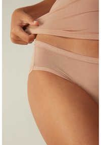 Beige nahtlose Unterwäsche mit weicher Textur, mittelhohem Bund und minimalen Nähten, kombiniert mit einem hautfarbenen Oberteil.