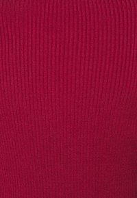 Gros plan sur un tissu maille côtelée rouge montrant des lignes texturées verticales, évoquant un pull ou un textile similaire.
