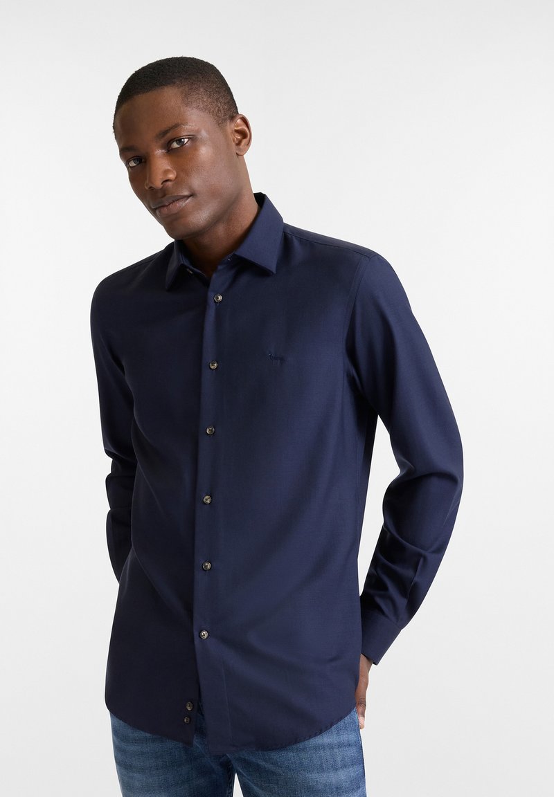 Navyblauwe longsleeve shirt van een gestructureerde stof, met een puntige kraag en knoopsluiting aan de voorkant met contrasterende knopen en subtiele logo-borduring.