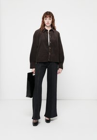 Cămașă button-up din cord închis cu mâneci lungi, asortată cu blugi negri evazați și o geantă de umăr neagră. Încălțămintea simplă completează look-ul.