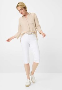 Camicia in lino beige chiaro con colletto, abbinata a pantaloni bianchi fino al ginocchio e sneakers bianche. L'outfit presenta un design semplice con minimi dettagli.
