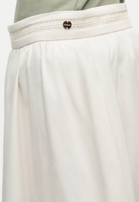 Κοντινό πλάνο λευκής φούστας με ρίγες, με διακοσμητική ζώνη μέσης που έχει δαντέλα και ένα μικρό στρογγυλό μεταλλικό κουμπί.