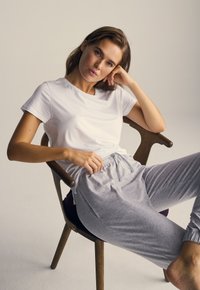 Hvid bomulds t-shirt og grå trækbånd bukser, begge bløde med en afslappet pasform, båret mens man sidder på en træstol.