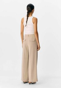 Breedbenige beige broeken met een soepele textuur, voorzien van twee achterzakken en een tailleband. Gecombineerd met een aansluitend wit tanktop.