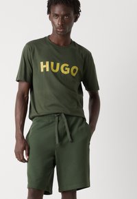 Grøn bomulds t-shirt med gyldent "HUGO" tekst, parret med matchende grønne shorts. Begge beklædningsgenstande har en afslappet pasform og blød tekstur.