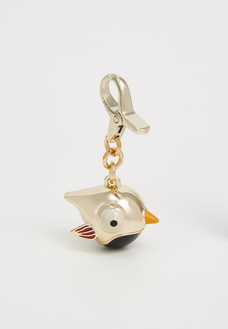 Breloc în formă de pasăre aurie cu un corp negru, un ochi alb, un cioc portocalie și accente de aripi roșii. Dispune de un clip metalic sigur pentru atașare.