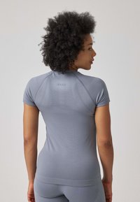 Top sportivo grigio a maniche corte, in tessuto strutturato e con cuciture raglan. Presenta un logo sulla parte superiore della schiena e una silhouette aderente.