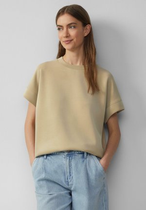 Beige sweatshirt met korte mouwen en een ronde halslijn, met een relaxed fit en een zachte textuur, gecombineerd met lichtblauwe denimspijkerbroek.