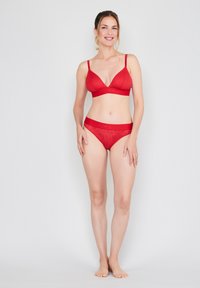Red bra and matching bikini, both with a wave pattern, featuring thin straps and an elastic waistband. Smooth texture and fitted design.