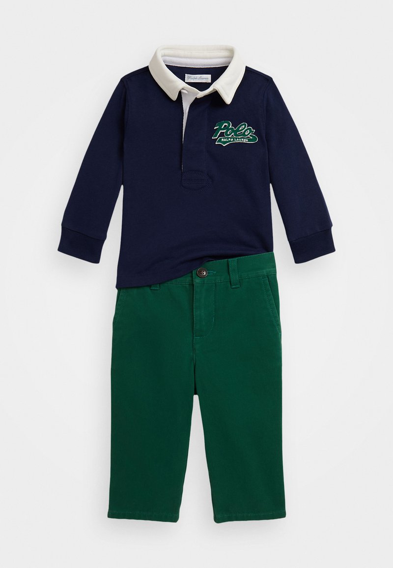 Jūrų mėlynumo ilgomis rankovėmis polo marškiniai su grietinėlės spalvos apykakle ir žalia „Polo Ralph Lauren“ logotipu, derinami su žaliais medvilniniais kelnais, turinčiais sagų užsegimą.