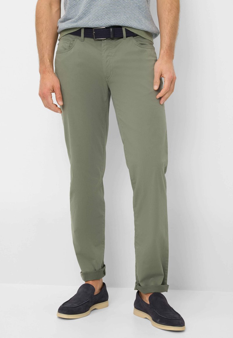Pantaloni in cotone leggeri di colore verde oliva, con una vestibilità slim. Presentano orli arrotolati e tasche frontali. Abbinati a scarpe scure senza lacci.
