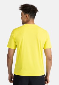 Gul kortärmad idrottströja med rundad halsringning och en slät yta, sedd bakifrån, ihop med svarta shorts.