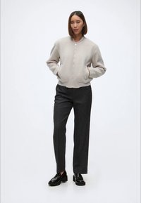 Beige glidelås fleece-jakke med ribbestrikket krage, kombinert med kullgrå bukser og svarte sko, med en avslappet passform og glatt tekstur.