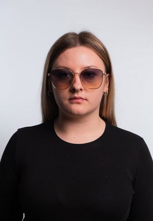 Occhiali da sole con montatura oversize, rotonda in metallo dorato, lenti sfumate marroni e parte frontale trasparente. Modello che indossa una maglietta nera a maniche lunghe.