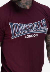 Bordovorý tričko Lonsdale London s bílým a námořnickým logem. Krátké rukávy a kulatý výstřih, vyrobené z měkké bavlny.
