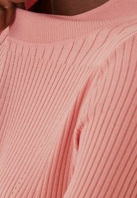 Roze ribgebreide trui met een ronde halslijn en een textuurpatroon, waarbij de zachte, rekbare stof en subtiele details worden benadrukt.