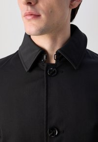 Cappotto nero con colletto, dotato di chiusura a un solo bottone e robusti ganci vicino al colletto per una chiusura sicura.