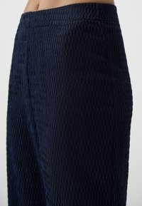 Marineblauwe textuurbroek met een gestructureerd ontwerp en een verheven patroon. De tailleband is elastisch en sluit strak aan.