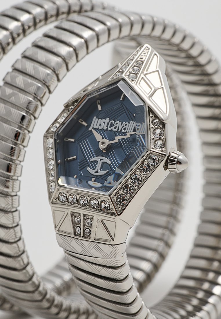 Montre octogonale argentée avec un cadran bleu à motif, entourée d'une lunette ornée de pierres. Dotée d'un bracelet en argent texturé.