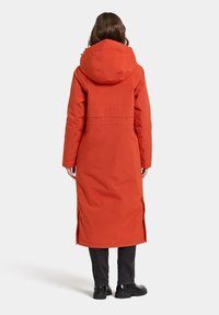 Long, orange puffer coat with a hood, featuring zippers at the sides, a cinched waist, and a durable, smooth exterior material.