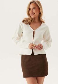 Haut crème à manches longues avec un décolleté en V et une fermeture à boutons. Assorti à une mini-jupe en daim marron. Texture lisse, design épuré.