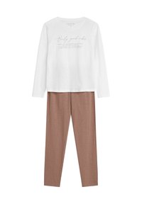 Biała koszula z długim rękawem z napisem "Tylko dobre wibracje", w połączeniu z jasnobrązowymi dopasowanymi spodniami, wykonanymi z miękkiego, gładkiego materiału.