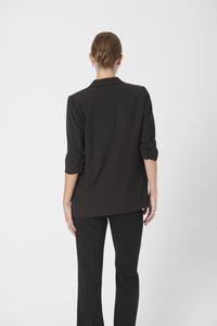 Blazer nero su misura con maniche arrotolate, caratterizzato da una texture liscia e un design strutturato. Abbinato a pantaloni neri dritti.