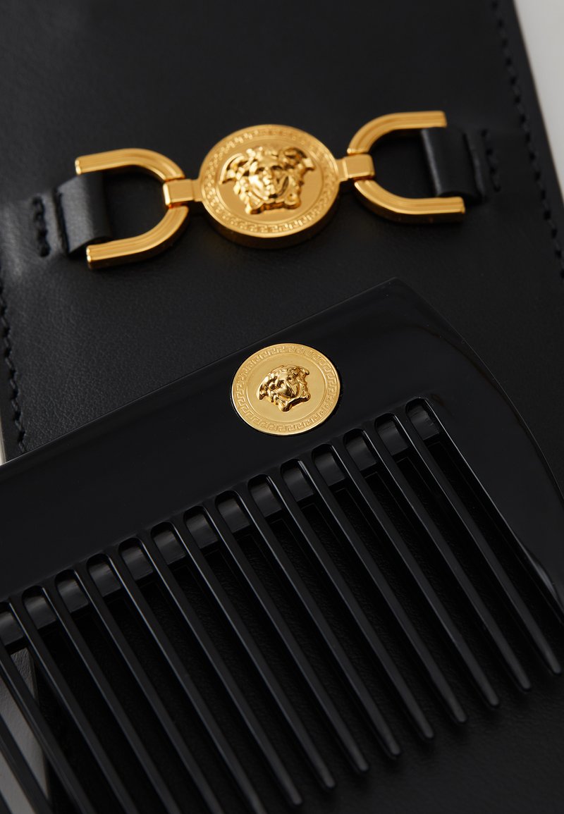 Schwarzer Kamm mit goldenen Akzenten und einem Löwenmedaillon, kombiniert mit einem schwarzen Lederetui, das mit einer goldenen Schnallendetail verziert ist.