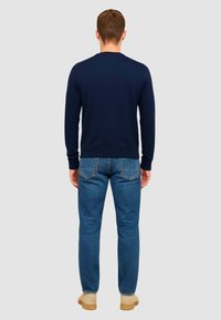 Maglione di lana blu navy con colletto rotondo, abbinato a jeans azzurri e scarpe beige; texture liscia e vestibilità classica.