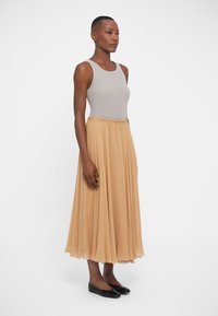 Gray ribbed tank top, flowing beige pleated midi skirt, and black flat shoes. Smooth textures, elastic waistband on skirt.