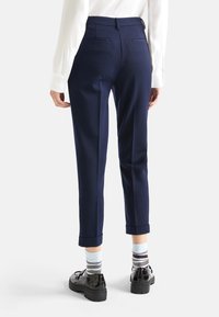 Marinblå byxor med skräddarsydd passform, med uppvikt fåll och två bakfickor, kombinerat med svarta skor och randiga strumpor.