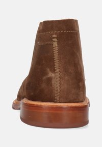 Brązowe zamszowe botki za kostkę o miękkiej fakturze, zaokrąglonym nosku i drewnianej podeszwie. Posiadają widoczny szew z tyłu oraz minimalistyczny design.