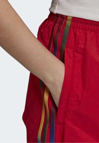 Červené sportovní kraťasy s elastickým pasem, s vertikálními vícebarevnými pruhy (zelená, žlutá, fialová, oranžová) po stranách.