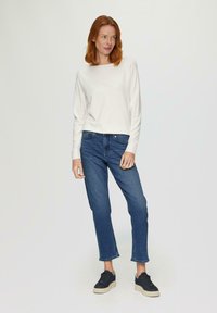 Witte lange mouwen top gecombineerd met blauwe jeans, met een losse pasvorm en een lichte manchet. Zwarte sneakers met een gestructureerde zool maken de look compleet.