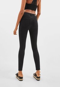 Jeans negros ajustados con una cintura alta, que cuentan con bolsillos traseros y un diseño elegante y ceñido. Acompañados de calzado ligero.