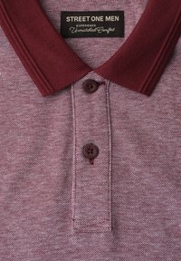 Polo bordeaux pour homme avec deux boutons et une étiquette indiquant "Street One Men Experience Unmatched Comfort."