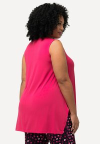 Fuchsia mouwloze top met een relaxte pasvorm, zachte textuur en ronde zoom. Gekoppeld met zwarte broek met een kleurrijk stippenpatroon.