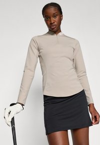 Maglietta beige a maniche lunghe con colletto a mezzo zip, abbinata a una gonna pantalone nera. Il tessuto sembra liscio, con un design aderente studiato per il comfort.