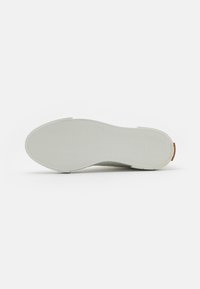 Sola de sapato branca de borracha com padrão de aderência texturizado, forma arredondada e design minimalista. Apresenta um pequeno detalhe laranja perto do calcanhar.