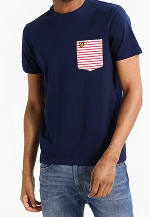 Marineblå bomuld t-shirt med en stribet lomme i rød og hvid, der har et lille gult logo. Rund hals og korte ærmer, afslappet pasform.