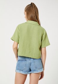 Korte mouwen, cropped shirt in een lichtgroene textuurstof met een kraag, in combinatie met lichtblauwe denim shorts met uitgesneden zoom.