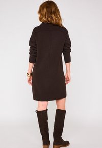 Vestito in maglia marrone con una parte superiore a coste e maniche aderenti, con un orlo solido. Indossato con stivali in suede marrone alti fino al ginocchio.