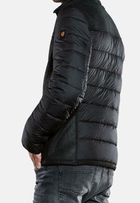 Mustapuffapuku, jossa on sileä, tikattu muotoilu ja teksturoitu kangas harteilla. Varustettu pienellä logolla vasemmassa hihassa.