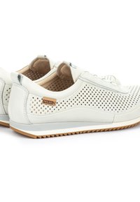 Sneaker bianche in pelle perforata con suola in gomma, dotate di un'etichetta in legno del marchio, design con lacci e accenti grigi a contrasto.