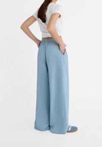 Losse lichtblauwe wijde broek met een elastische tailleband, zijzakken en een gladde, licht gestructureerde stof.