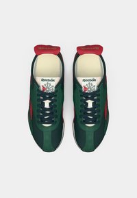 Par de sapatilhas Reebok em verde escuro e vermelho com atacadores pretos, solas interiores brancas e logótipo da Reebok na lingueta, vistas de cima.