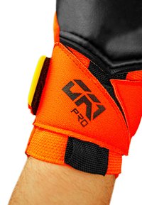 Soutien de poignet orange vif avec des accents noirs, comportant un tissu texturé, un logo et une fermeture Velcro réglable pour un ajustement sécurisé.