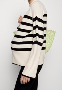 Černobíle pruhovaný svetr vyrobený z měkké látky, s dlouhými rukávy a volným střihem, doplněný o texturovanou zelenou tašku.