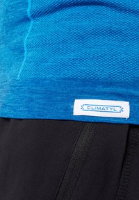 Maglietta sportiva blu con un design a maglia testurizzata. Orlo rifinito con un'etichetta bianca che reca la scritta "CLIMATYL". Abbinata a pantaloni corti neri.