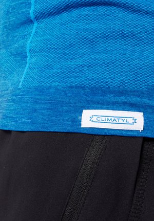 Maglietta sportiva blu con un design a maglia testurizzata. Orlo rifinito con un'etichetta bianca che reca la scritta "CLIMATYL". Abbinata a pantaloni corti neri.